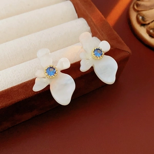 Détail de boucles d'oreilles fleurs en résine avec zircon bleu dans un écrin en velours