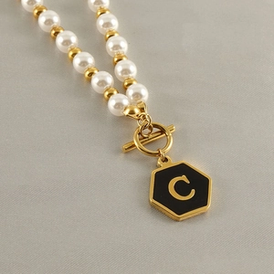 Close-up of pearl and gold bead necklace with a black hexagon pendant engraved with letter C