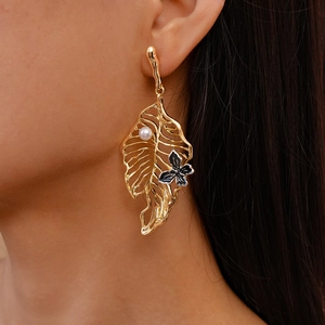 Close-up of golden hollow leaf earrings with white pearl and dark butterfly on model