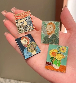 Detail of four Van Gogh and Munch enamel pins held in hand to show size and texture