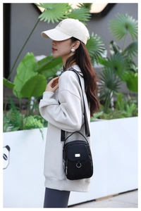 Detail of a black nylon crossbody bag with silver hardware on a casual female model