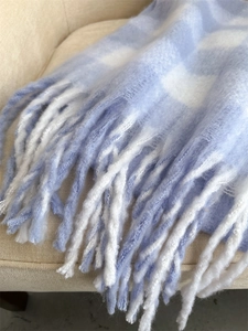 Detail of light blue and white checkered scarf with soft fringe and wool-like texture