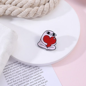 Detail shot of a cute pink cartoon enamel pin holding a red heart on a white display