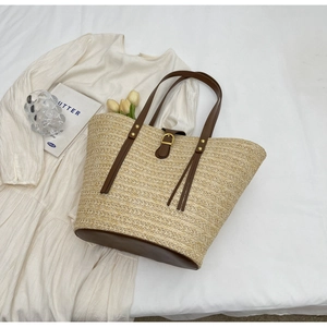 Close-up of a large straw beach tote bag featuring brown leather straps and metal buckle