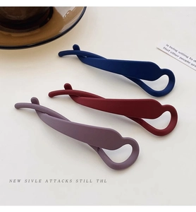Three matte twist banana hair clips in navy, burgundy, and purple-grey on a minimalist desk