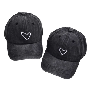 Detail van twee zwarte distressed baseballpetten met wit hartje borduursel