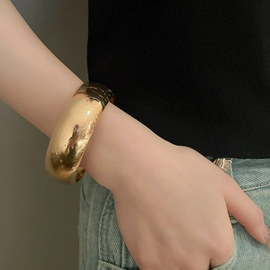 Close-up of chunky gold-colored metal cuff bracelet featuring bold floral heart design