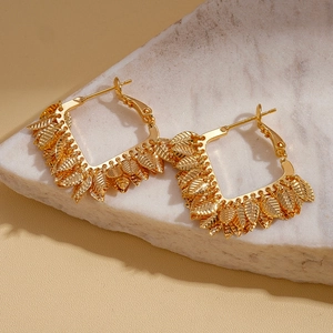 Détail de créoles plaquées or 18 carats avec pompons de feuilles sur marbre