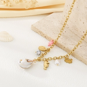 Gold stainless steel necklace with pearl, seashell and starfish charms on a sandy beach