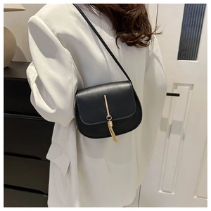 Detailed view of a black leather saddle bag featuring a long gold metal tassel charm