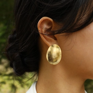 Golden brushed metal oval earrings in minimalist crumpled style on female model