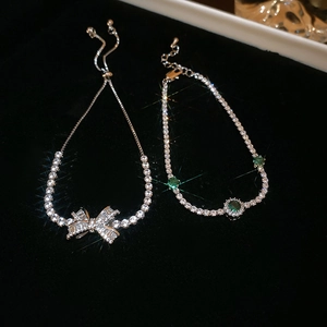 Close-up of sparkling zircon bow bracelet and green gemstone on black velvet background