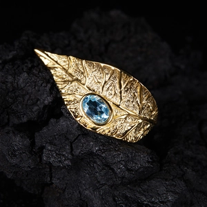 Macro detail of leaf shaped gold ring featuring an oval blue gemstone on charcoal