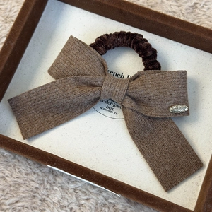 Macro shot of brown knit bow scrunchie with Love is forever metal tag detail