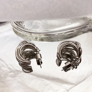 Macro detail of silver multi-layer woven C-shape hoop earrings on white textured fabric