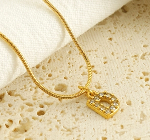 Macro view of gold snake chain necklace featuring a crystal-encrusted letter D pendant
