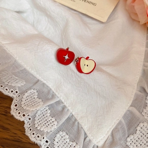 Macro shot of asymmetric red apple stud earrings with crystals on white lace fabric