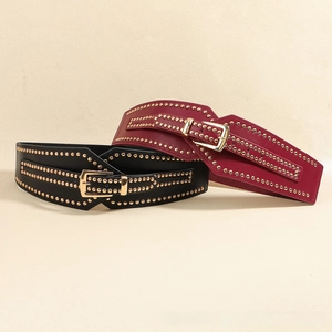 Detail of wide elastic belts featuring gold metal studs and polished buckles in black and burgundy