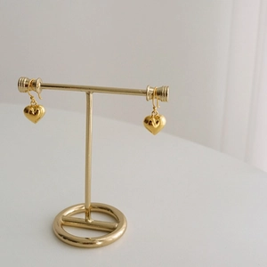 Detail of golden heart-shaped dangle earrings displayed on a T-bar jewelry stand