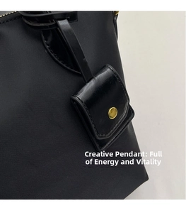 Detail of black nylon tote bag featuring a leather strap attachment with a gold snap button