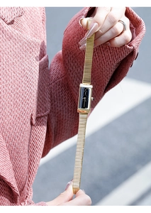 Close-up of elegant gold rectangular ladies watch with black dial and mesh strap