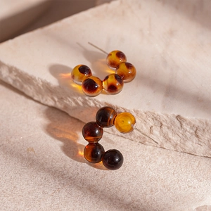 Close-up of tortoiseshell resin beaded C-shaped hoop earrings on beige stone texture