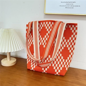 Detail of knitted tote bag with orange and white checkerboard pattern on a wooden table