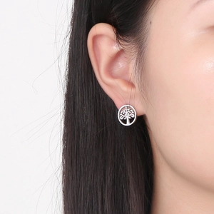 Close-up of silver stainless steel Tree of Life hollow stud earrings on female ear