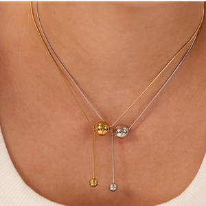 Close-up of gold and silver ball pendant snake chain necklaces on model's neck