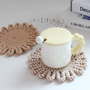 Detail of woven cotton flower-shaped trivets in khaki and white on a white desk