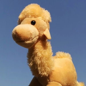 Detailed view of soft yellow camel plush toy against a clear blue sky background