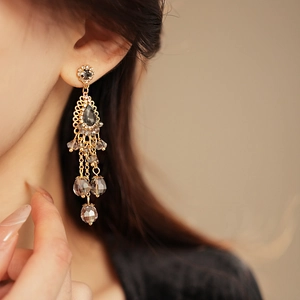 Close-up of bohemian gold tassel earrings with dark teardrop crystals on a model