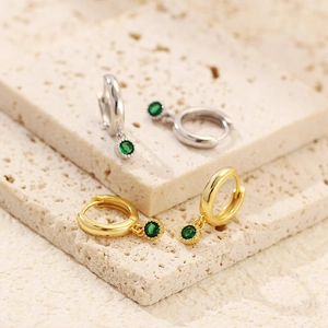 Detail of s925 silver hoop earrings with green gemstone pendants on a textured stone