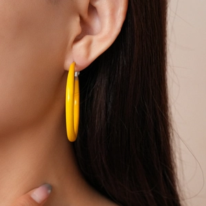 Close-up of a model wearing bright yellow geometric round hoop earrings in polished metal