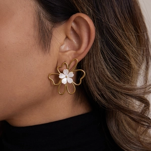 Close-up of elegant gold flower stud earrings with pearl centers worn by a model
