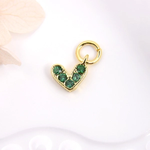 Macro shot of heart-shaped gold charm with green cubic zirconia on white background