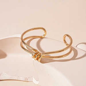 Detail of gold double-layer knotted open bangle on a minimalist white stone background