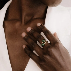 Detailed close-up of a double pear-cut emerald green stone ring on a golden band