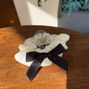 Detail of cream pleated scrunchie with a black satin bow and integrated claw clip