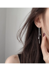 Close-up of silver chain earrings with star, cross and bar charms on a model