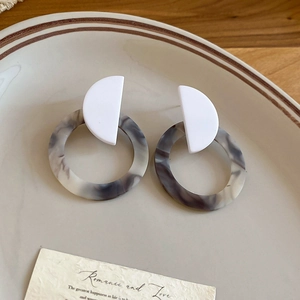 Detail showing marble resin drop earrings with geometric shapes on a ceramic plate