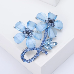 Detail of blue alloy flower brooch with rhinestone crystals on a white pedestal