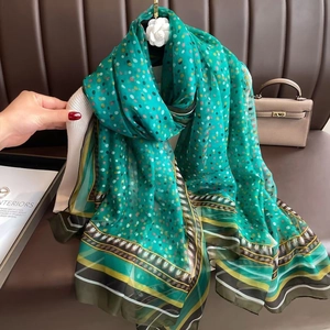 Detail of a green polka dot silk scarf held by hand featuring geometric print and soft fabric