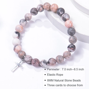 Detail view of pink zebra stone beaded bracelet with metal cross charm on white surface