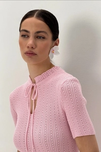 Dettaglio di top in maglia rosa con uncinetto traforato e collo a balze con lacci