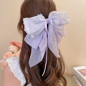 Dettaglio della molletta in organza viola con ricamo floreale e lunghi nastri a nappa