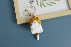 Close-up of handmade orange and white knitted cat keychain with gold metal hardware