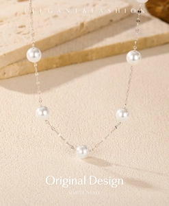Elegant silver chain necklace with round white pearls on a minimalist textured surface
