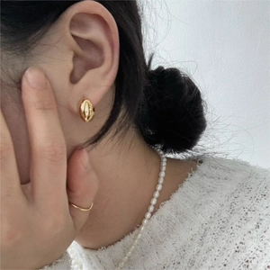 Close-up of minimalist golden oval stud earrings on a model for an elegant aesthetic