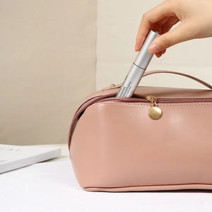 Pink PU leather accordion makeup bag shown with hand placing mascara inside for storage